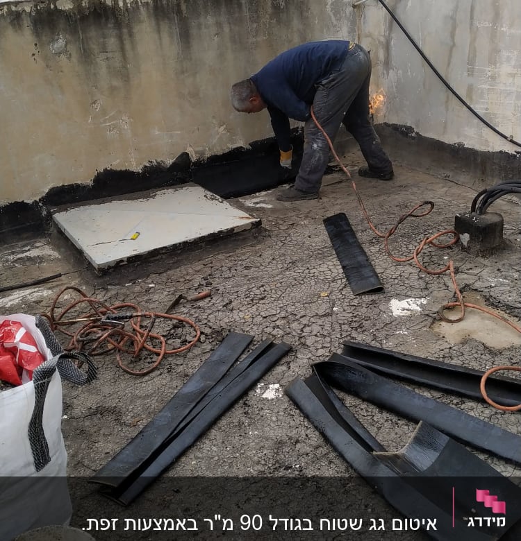 אדם עובד על איטום גג עם יריעות ביטומניות.